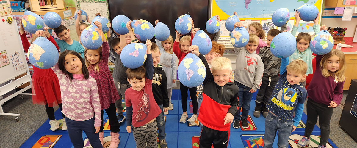 Kindergarteners smile big while holding balloons.