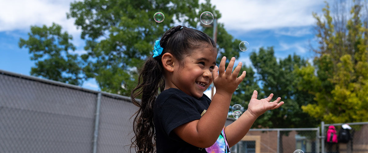 A preschooler blows bubbles on the playground. 