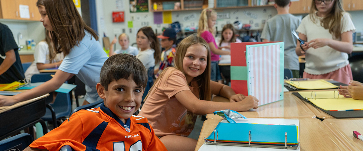 Two middle school students at their desks smiling at the camera.