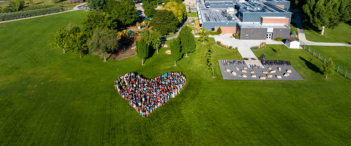 A drone shot of Zach Elementary with a heart-shape of people and mountains in the background,