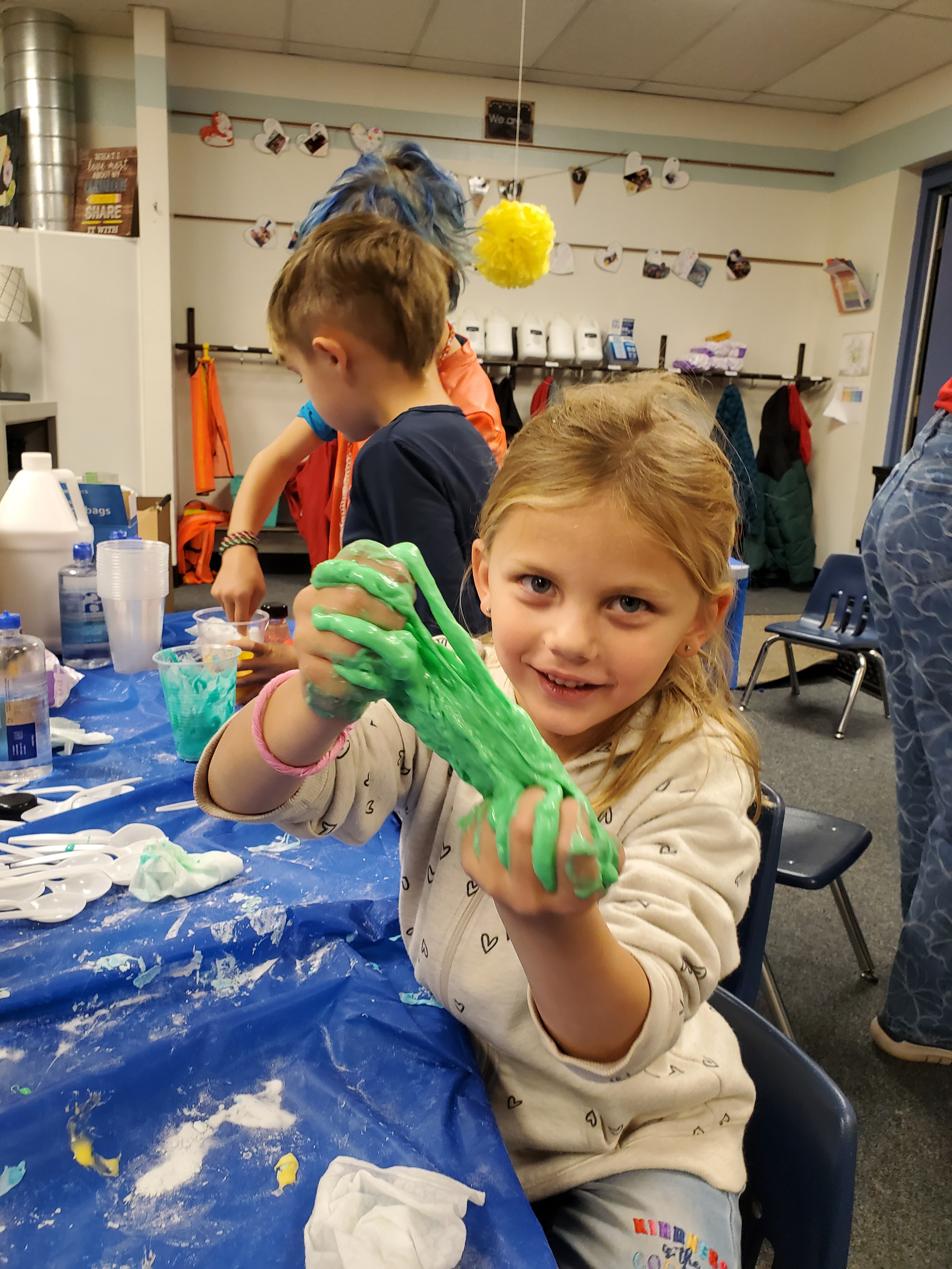 A young girl holds her green slime out to the camera. 