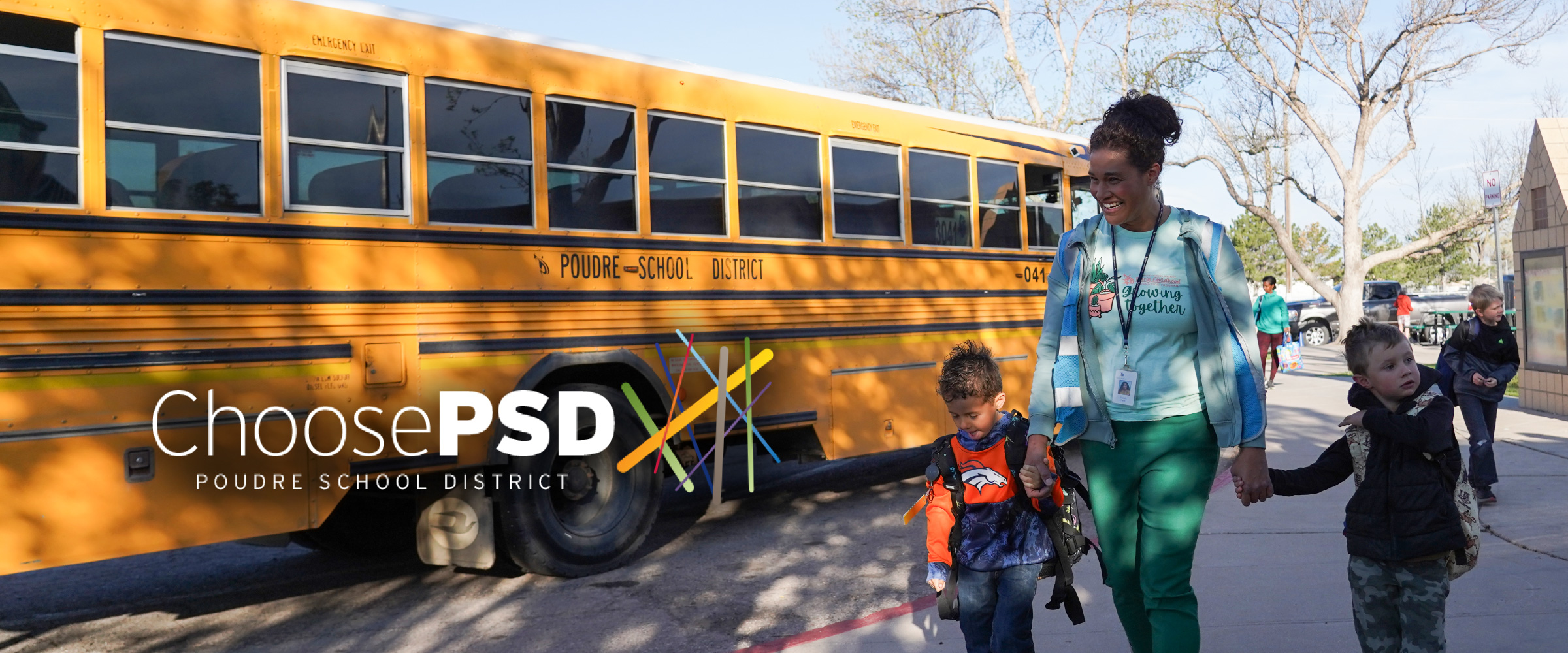 A PSD staff member leading two young children from the bus to school