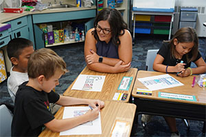 Teacher with students at classroom desks. 