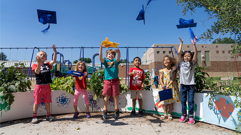 Kindergarteners jump and throw graduation caps in the air.