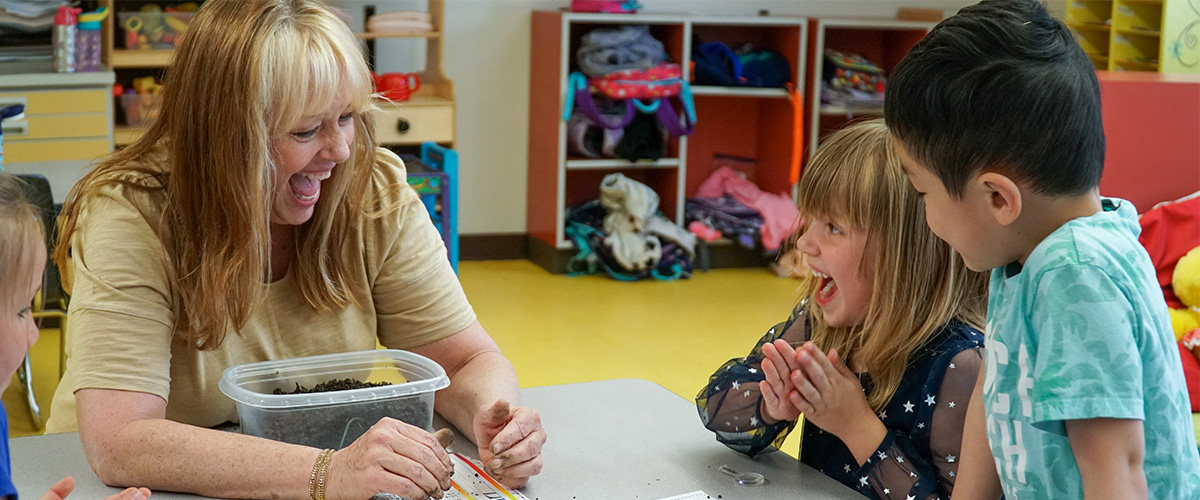 A kindergarten teacher laughs with students. 