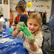 A girl holds her green slime out to the camera.