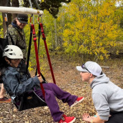 A physical education teacher encourages a student using an adaptive climbing harness.