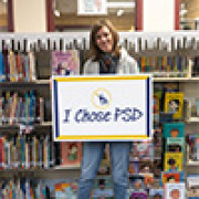 Annie Herzig holds a "I chose PSD" sign in a school library. 